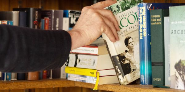 Das Foto zeigt eine Hand, die ein Buch aus einem Offenen Bücherregal entnimmt